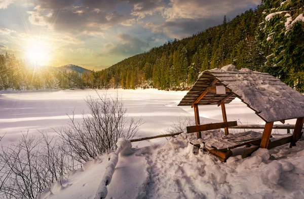 wooden bower in snowy winter forest at sunset