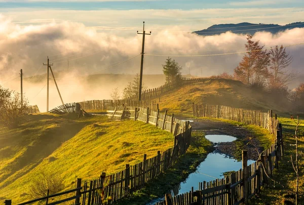 Сельская дорога среди деревянных заборов в утреннем тумане — стоковое фото