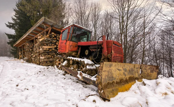Roter Planierraupe im Schnee neben dem Holzschuppen — Stockfoto