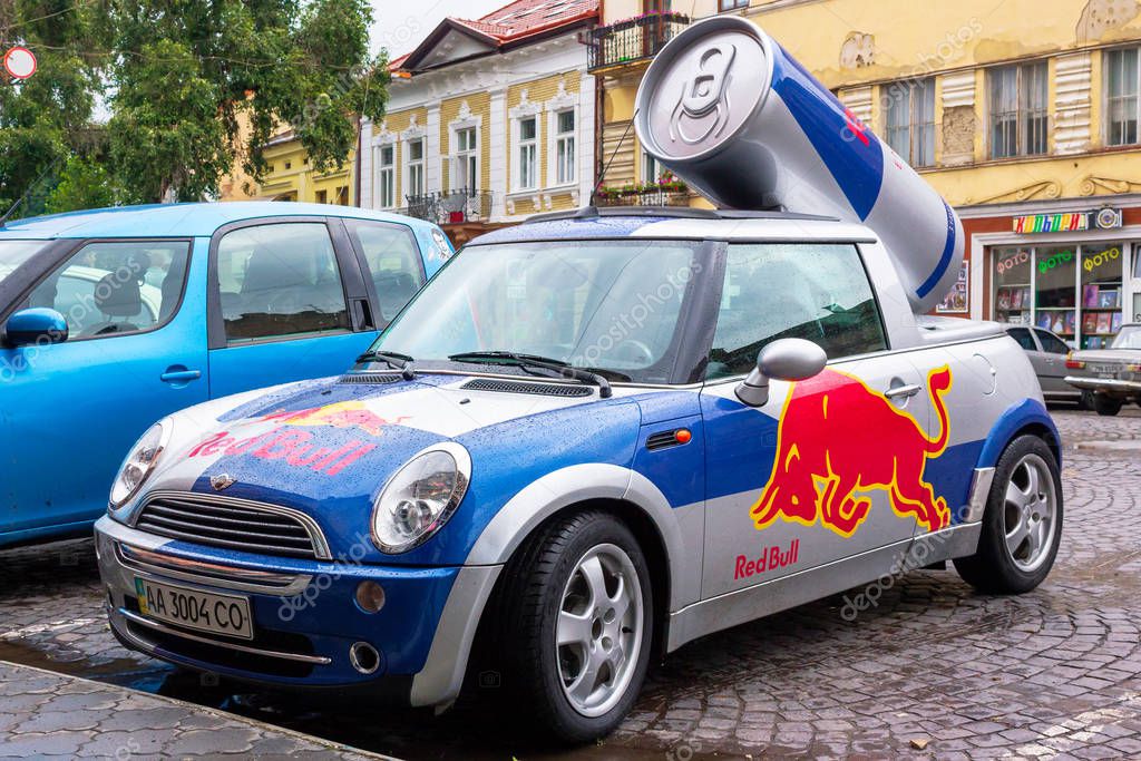 Uzhhorod, ukraine - 14 JUL, 2013: Red Bull mini cooper publicity car with a can of energy drink behind. fancy car tuning used for promotion. wet advertisement vehicle after the rain