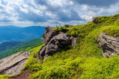 Dağın tepesinden vadiye bak. Çimenli yamaçtaki dev kayalar. Gökyüzündeki bulutlar. Işıklı güzel güneşli bir hava. Turizm kavramında özgürlük