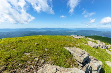 Alp çayırındaki kayalar. Runa Dağı 'nın güzel yaz manzarası. Uzakta kırsal vadi var. Mavi gökyüzünde kabarık bulutlarla harika bir hava.