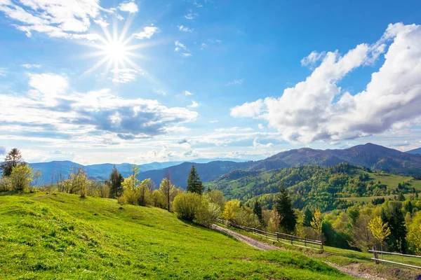 令人叹为观止的山地乡村风景 乡间小路穿过田野和山丘上的草地 滚向远方的山脊 春天阳光灿烂的日子里的自然景观 天空中的太阳和蓬松的云彩 — 图库照片