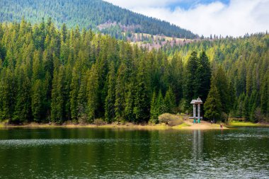 Ormanın içindeki dağlık dağ gölü. Mavi gökyüzünde yumuşak bulutları olan güzel güneşli bir hava. İlkbahar manzarası benekli ışıkta. Synevyr Ulusal Parkı, Ukrayna 'da su kütlesi
