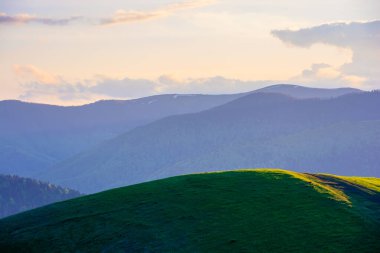 İlkbaharda alacakaranlıkta dağlık kırlarda. Yuvarlanan tepeler boyunca yol. Uzakta tepe var. Gökyüzündeki bulutlar. Karpatların güzel kırsal manzarası