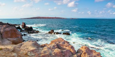 Kayalıklı ve kayalıklı deniz manzarası. Öğleden sonra ışığında güzel bir manzara. Uzakta bir ada. Akşam gökyüzünde kabarık bulutlar. Uzakta St. Ivan ve St. Peter Adası var.