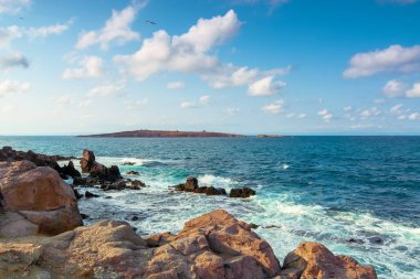 Kayalıklı ve kayalıklı deniz manzarası. Öğleden sonra ışığında güzel bir manzara. Uzakta bir ada. Akşam gökyüzünde kabarık bulutlar. Uzakta St. Ivan ve St. Peter Adası var.