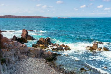 Kayalıklı ve kayalıklı deniz manzarası. Öğleden sonra ışığında güzel bir manzara. Uzakta bir ada. Akşam gökyüzünde kabarık bulutlar. Uzakta St. Ivan ve St. Peter Adası var.