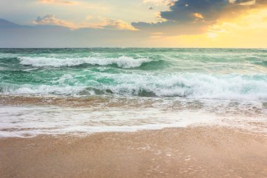 Güneş doğarken kumlu sahilde fırtına. Bulutlu gökyüzü ile dramatik okyanus manzarası. Sabah ışığında dalgalar ve dalgalar.