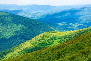 Yazın harika bir dağ manzarası. Taze yeşil ve mavi renklerde güzel bir doğa. Bulutlu bir gökyüzünün altındaki benekli ışıkta harika bir dağ manzarası.