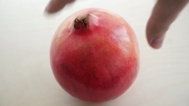 Erkek El, ahşap bir yüzeyde olgun kırmızı bir nar döndürüyor, yakın plan.