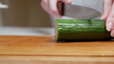 Modern bir mutfakta, tahta bir tahtanın üzerinde salatalık kesen kadın ellerine yakın çekim. Sağlıklı beslenme. Makro. Salata hazırla.