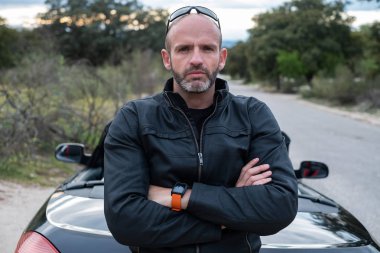 Sakal, deri ceket, güneş gözlüğü ve Cabrio arabasının arka içinde portakal izle olan bir orta-yaş kel adam portresi