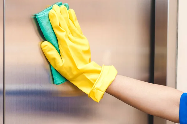 A hand in a yellow rubber glove washes the lift with a green rag