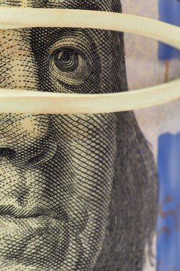 Yeni numunenin 100 dolarlık renginin bir parçası çok yakın planda. Franklin 'in yüzü maskeli. Görüntü dikey odaklı. Kayıt dışı para masanın altında. Birincil yedek para birimi. Makro