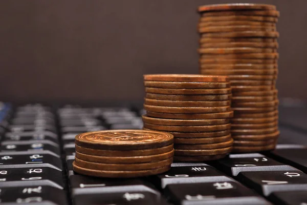 Piles of Japanese ten yen coins stand on a black computer or laptop keyboard. Behind them is a dark brown background. Online trading, payments and remote work. Close-up