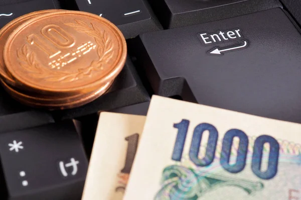 Japanese money is on the black keyboard of a computer or laptop near the Enter button. 100 yen coin and 1000 yen bill. Online trading, e-commerce and payments. Macro