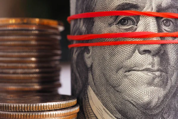 Bir paket eski usul 100 dolarlık banknot Amerikan çeyrekliklerinin yanında. Banknotlar toplanır ve elastik bir bantla bir araya getirilir. Gösterişsiz bir şekilde dramatik bir illüstrasyon. Kayıt dışı para. Makro