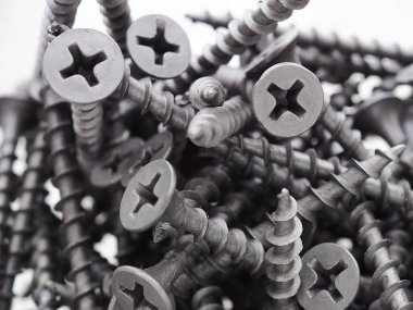 Bir sürü siyah büyük vida beyaz arka planda bir yığın içinde yatıyor. Yakın plan. Donanım, bağlayıcılar, demir teçhizat, demircilik, inşaat ve onarım malzemeleri. Makro