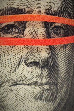 100 dolarlık banknot çok yakın. Franklin 'in yüzü maske gibi lastik bir bantla kaplı. Amerikan ekonomisi ve devalüasyonuyla ilgili haberler. Gözetleme, sade anahtar. Dikey çekim. Makro