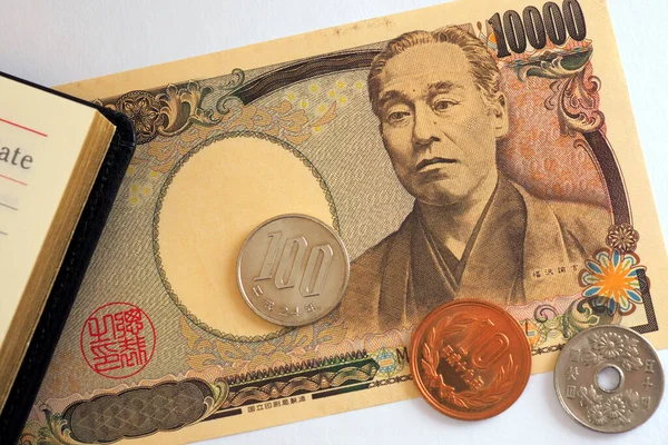 日本のお金 硬貨が日記の近くにある ホワイトペーパーの背景に10000円紙幣のクローズアップ 経済や銀行に関するニュース 財務管理と意思決定 マクロ — ストック写真