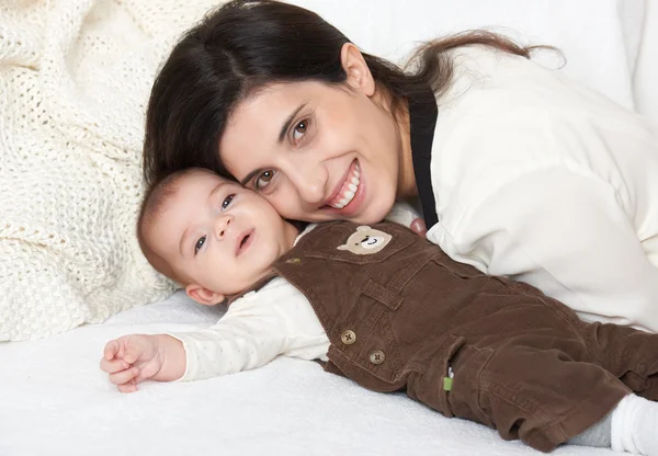 Madre se acuesta con el bebé en la cama, retrato familiar feliz sobre fondo blanco — Foto de Stock