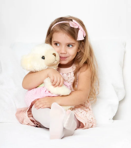 Adorable little child girl sit in the bed with her toy. The child girl hugs the teddy bear. — Stock Photo, Image