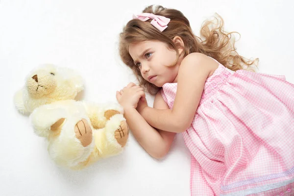 Arg tjej barn med nallebjörn Ligg på vit handduk i sängen, klädd i rosa — Stockfoto