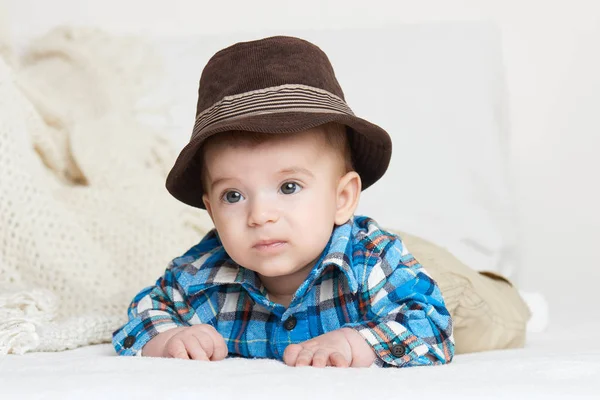 Baby portrait lie on white towel in bed, dressed in plaid shirt and hat — Stock Photo, Image