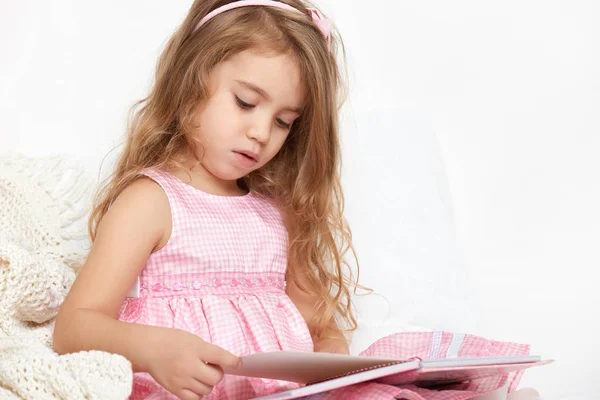 Dívka dítě rad kniha v posteli, oblečená v růžovém — Stock fotografie