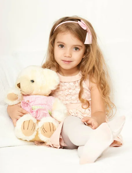 Adorable little child girl sit in the bed with her toy. The child girl hugs the teddy bear. — Stock Photo, Image