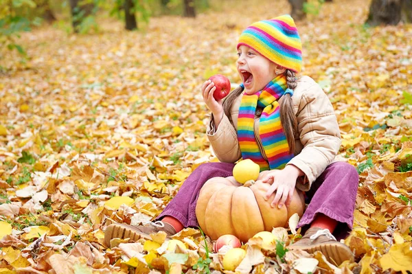 Niña en el bosque de otoño, sentarse en hojas amarillas, comer manzana y calabaza — Foto de Stock