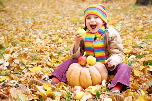 Girl child in autumn forest, sit on yellow leaves, eat apple and pumpkin — Stock Photo, Image