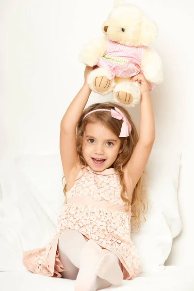 Adorable little child girl sit in the bed with her toy. The child girl hugs the teddy bear. — Stock Photo, Image