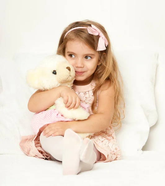 Entzückende kleine Mädchen sitzen im Bett mit ihrem Spielzeug. das kleine Mädchen umarmt den Teddybär. — Stockfoto