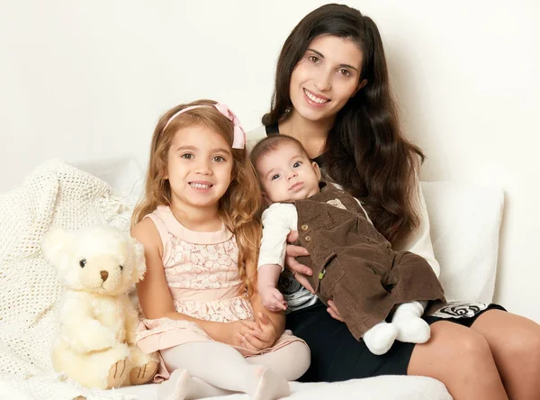 Mãe com seus filhos sentar na cama com ursinho de pelúcia, retrato de família feliz — Fotografia de Stock