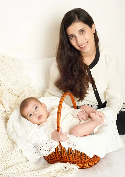 Mãe com bebê na cesta na cama, retrato de família feliz no fundo branco, amarelo tonificado — Fotografia de Stock