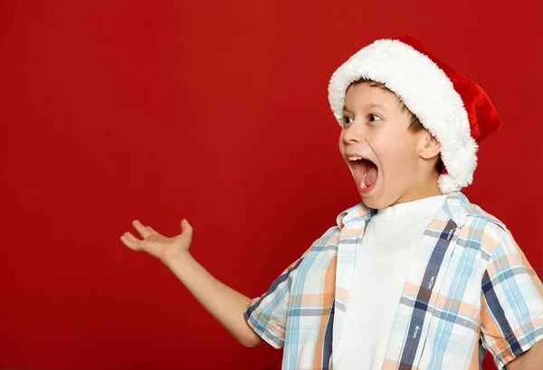 Enfant garçon portrait en santa chapeau sur rouge, avoir du plaisir et des émotions, concept de vacances d'hiver — Photo