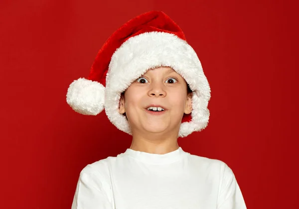 Здивований хлопчик дитячий портрет в капелюсі Санта на червоному, розважається і емоції, концепція зимового свята — стокове фото