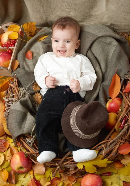 Otoño niño se acuesta sobre hojas de otoño amarillo, manzanas, calabaza y decoración en textil — Foto de Stock