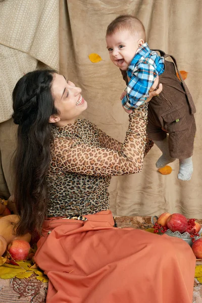 Autunno donna con bambino su foglie di autunno giallo, mele, zucca e decorazione su tessile, famiglia felice e concetto di paese — Foto Stock