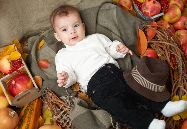 Otoño niño se acuesta sobre hojas de otoño amarillo, manzanas, calabaza y decoración en textil — Foto de Stock