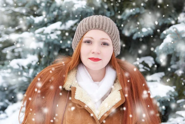 Wanita cantik di luar ruangan musim dingin, pohon cemara bersalju di hutan, rambut merah panjang, mengenakan mantel kulit domba — Stok Foto