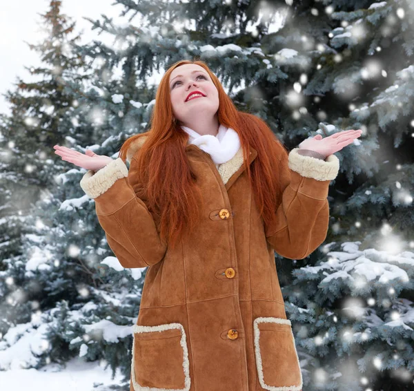 Hermosa mujer en invierno al aire libre, abetos nevados en el bosque, pelo largo y rojo, con un abrigo de piel de oveja — Foto de Stock