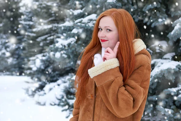 Hermosa mujer en invierno al aire libre, abetos nevados en el bosque, pelo largo y rojo, con un abrigo de piel de oveja — Foto de Stock