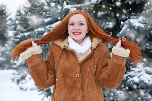 Hermosa mujer en invierno al aire libre, abetos nevados en el bosque, pelo largo y rojo, con un abrigo de piel de oveja — Foto de Stock
