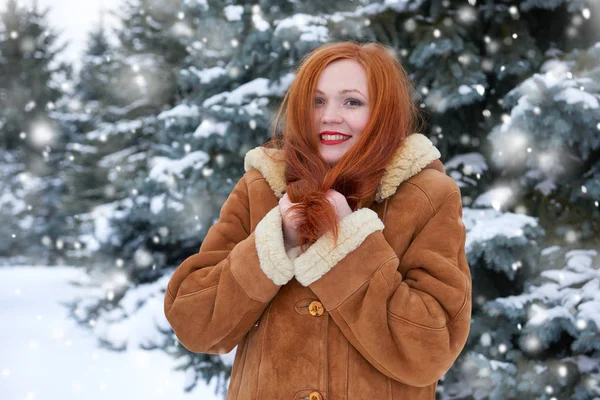 Beautiful woman on winter outdoor, snowy fir trees in forest, long red hair, wearing a sheepskin coat — Stock Photo, Image