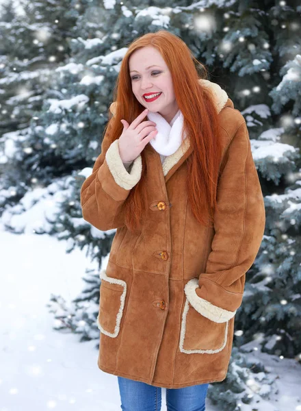 Hermosa mujer en invierno al aire libre, abetos nevados en el bosque, pelo largo y rojo, con un abrigo de piel de oveja — Foto de Stock