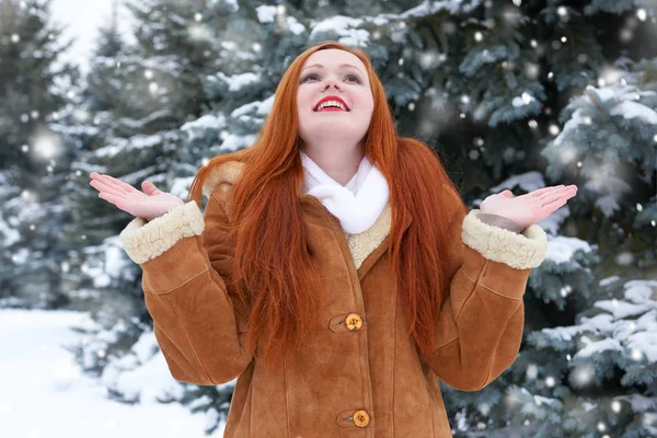 Hermosa mujer en invierno al aire libre, abetos nevados en el bosque, pelo largo y rojo, con un abrigo de piel de oveja — Foto de Stock