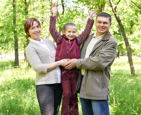 Šťastná rodina s dítětem v létě park, sluneční světlo, zelené trávy a stromy — Stock fotografie